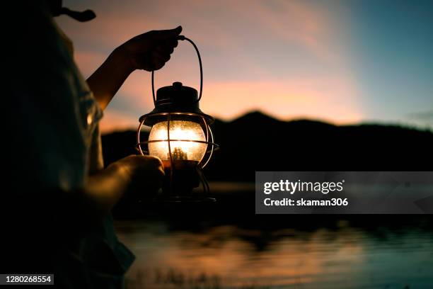 close up traveler hand holding vintage lantern and lighting for camping outdoor with twilight sunset background - lanterne photos et images de collection