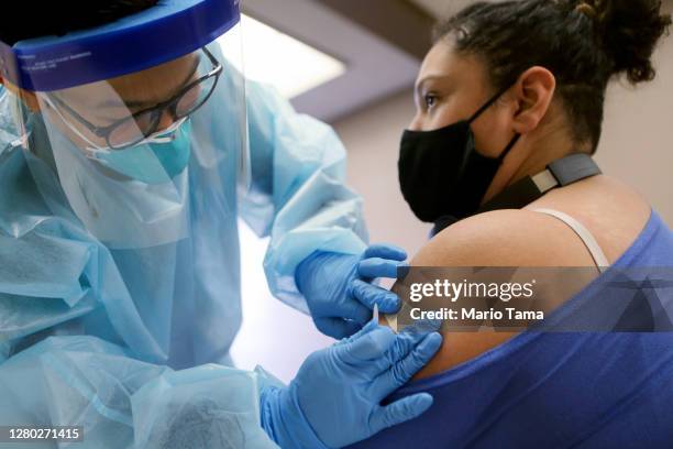 Nurse applies a band- aid after administering the flu vaccination shot to a woman at a free clinic held at a local library on October 14, 2020 in...