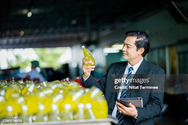 portrait of businessman owner holding product of a basil seed with pineapple fruit flavors bottles and holding digital tablet in production process. food and beverage industry business. - food and drink industry fotografías e imágenes de stock