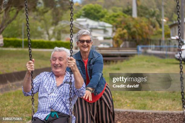 aktives seniorenpaar spielt auf einer schaukel im park - schaukel frau stock-fotos und bilder