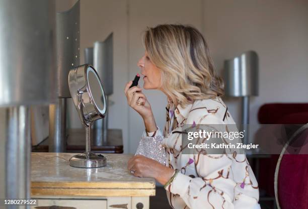 profile view of beautiful mature woman at dressing table, applying lipstick - sequin blouse fotografías e imágenes de stock