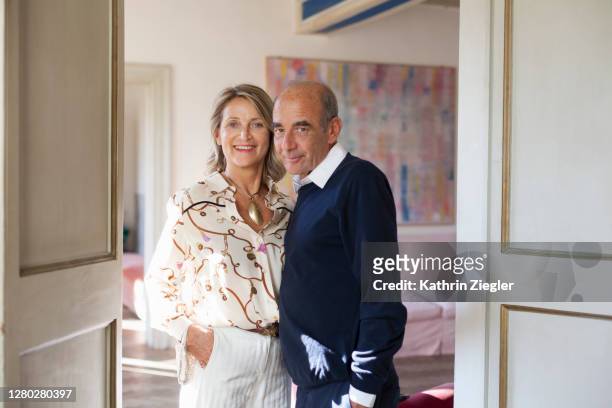 mature couple in the doorway of their beautiful apartment, looking at camera - house for an art lover stock pictures, royalty-free photos & images