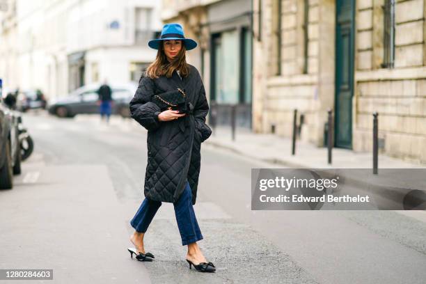 Therese Hellström wears a blue hat from Bronte, a black quilted Chanel bag with golden chain, a black padded puffer long coat from Custommade, blue...
