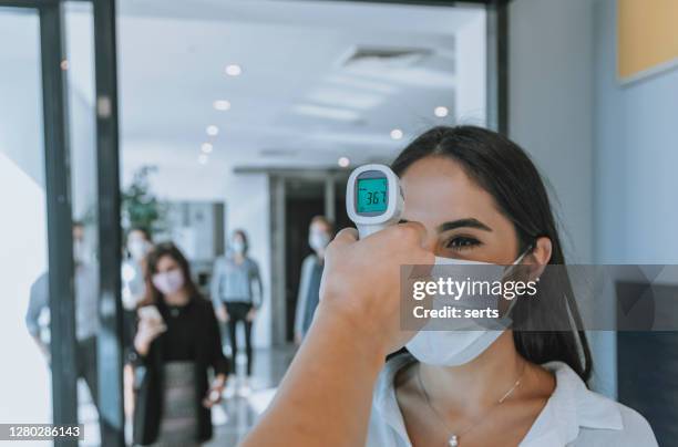 büroangestellter, der die temperatur von geschäftsleuten mit gesichtsmaske auf pandemie misst, während mitarbeiter ins büro zurückkehren - fieberkontrolle stock-fotos und bilder