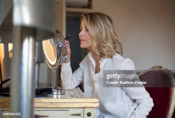 beautiful mature woman at dressing table, applying lipstick - vanity table stock pictures, royalty-free photos & images