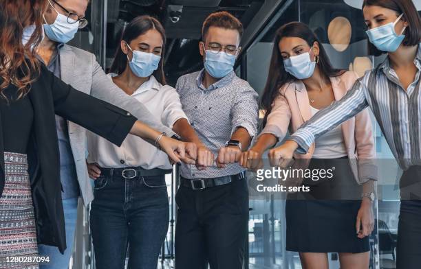 team of colleagues with face mask joining their hands together in unity during pandemic - covid greeting stock pictures, royalty-free photos & images