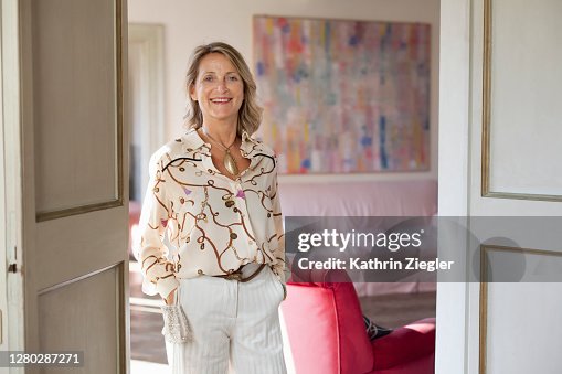 Portrait of an elegantly dressed mature woman in her beautiful apartment, wearing protective face mask around her wrist Portrait of an elegantly dressed mature woman in her beautiful apartment, wearing protective face mask around her wrist