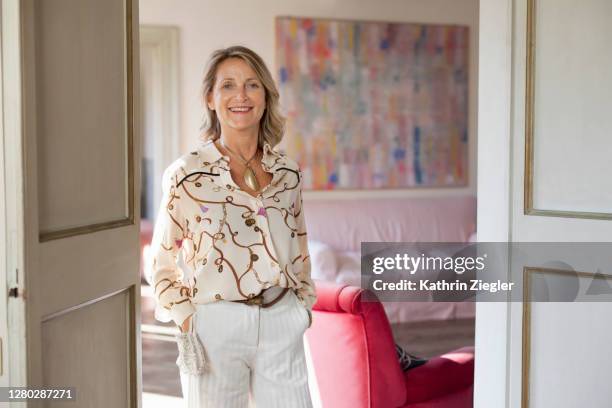 portrait of an elegantly dressed mature woman in her beautiful apartment, wearing protective face mask around her wrist - white blouse stock pictures, royalty-free photos & images