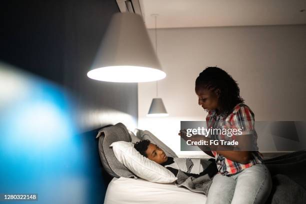 mother taking temperature and taking care of her sick son at home - hot latin nights stock pictures, royalty-free photos & images