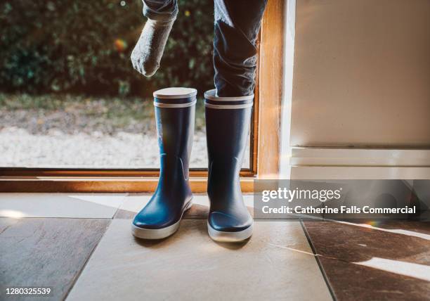 child putting on blue wellington boots - ゴム長靴 ストックフォトと画像