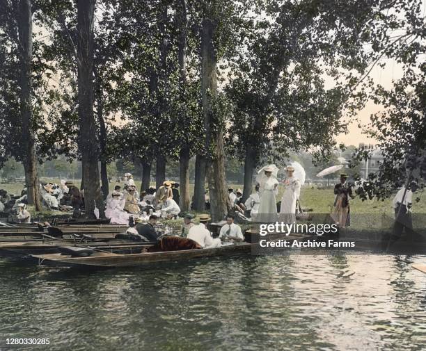 Colorized photo of well-dressed attendees, in punts and on the shores of the Thames, during the Henley Royal Regatta, Henley-On-Thames, Oxfordshire,...