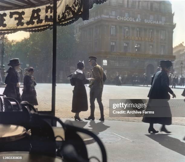 Colorized photo of a woman and a uniformed soldier as they stand close together, in front of Cafe de la Paix on the Boulevard des Capucines, Paris,...