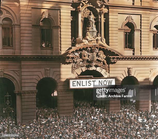 Colorized view of a crowd gathered in Martin Place for a WWI Recruitment Rally, Sydney, Australia, 1917. A sign reading 'Enlist Now' hangs above the...