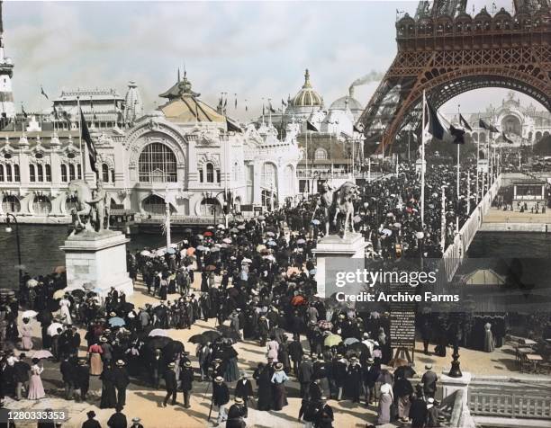 Colorized, high-angle view of exhibition visitors on the Pont d'Iena, under the base of the Eiffel Tower and stretching along the Champ de Mars at...