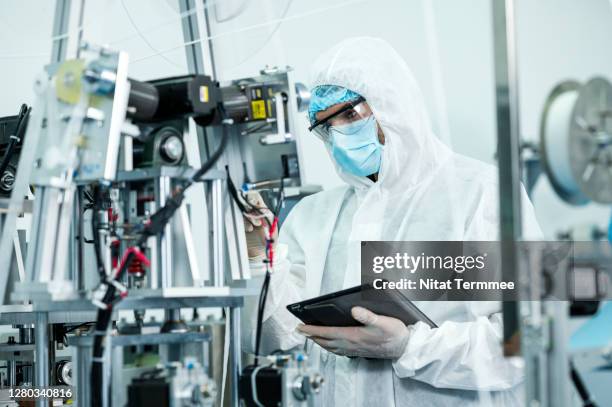 shot of production line worker wearing face mask and clean suit coveralls working in electronic factory. - chip fabrik stock-fotos und bilder