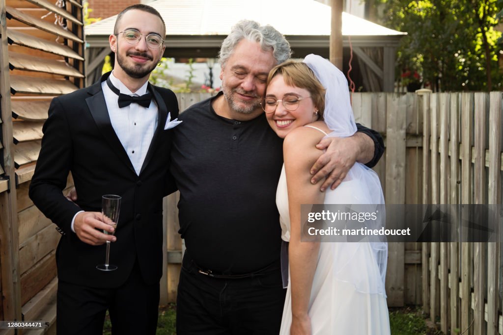 Millennial frisch vermählte paar posiert mit Vater der Braut im Hinterhof.