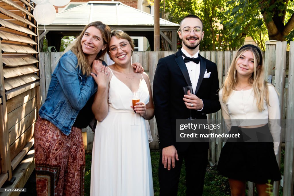Casal recém-casado millennial posando com membros da família no quintal.