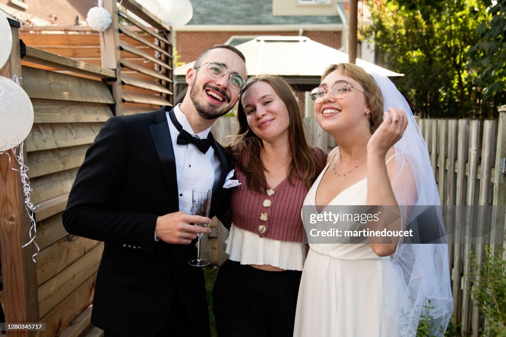 Millennial newlywed couple posing with bridesmaid in backyard.