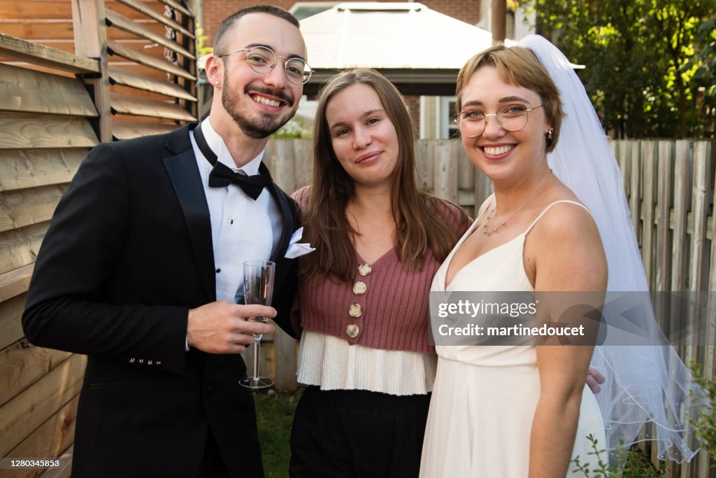 Millennial pareja recién casada posando con dama de honor en el patio trasero.