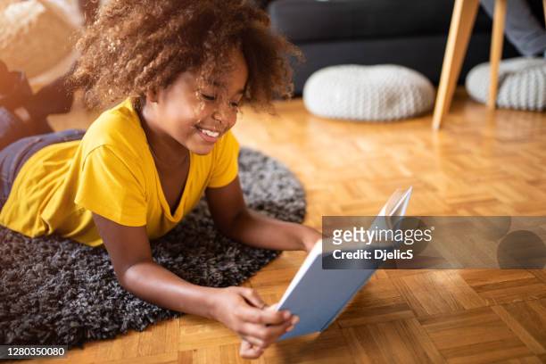 una chica feliz leyendo un libro en la sala de estar. - reading fotografías e imágenes de stock