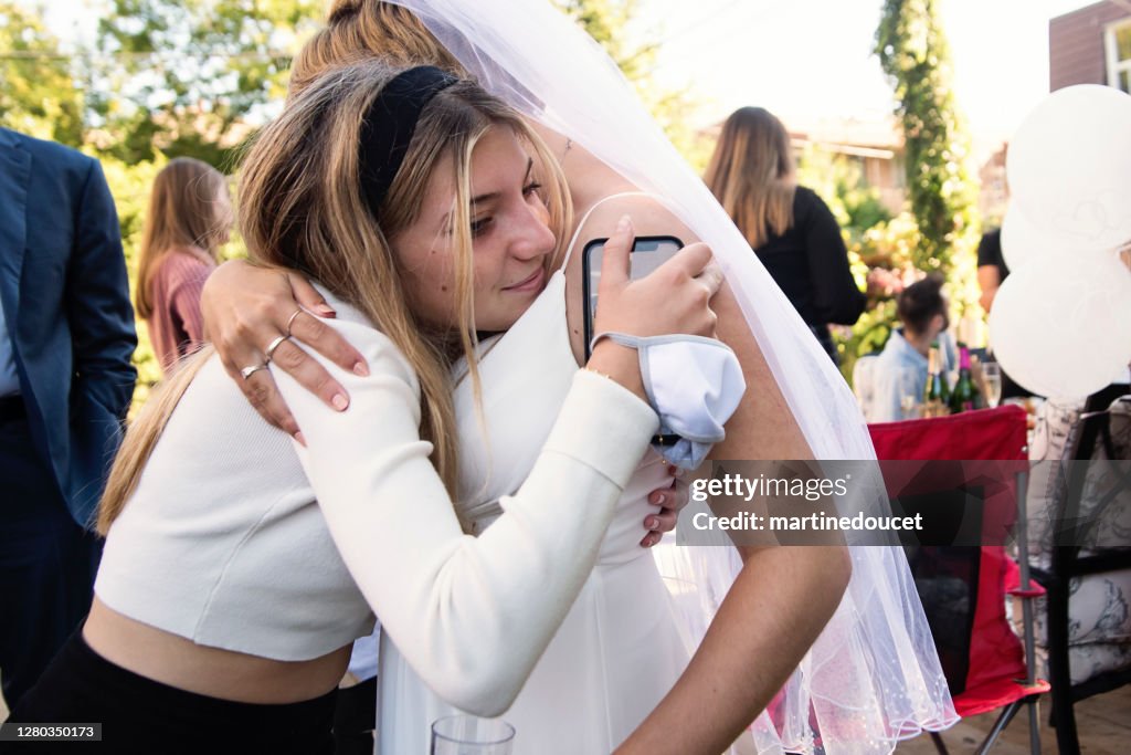 Millennial bride hugging cousin at wedding cocktail in backyard.