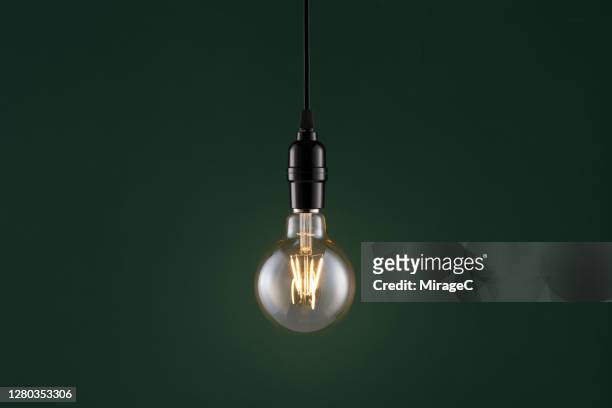 retro style light bulb on dark green - filamento fotografías e imágenes de stock