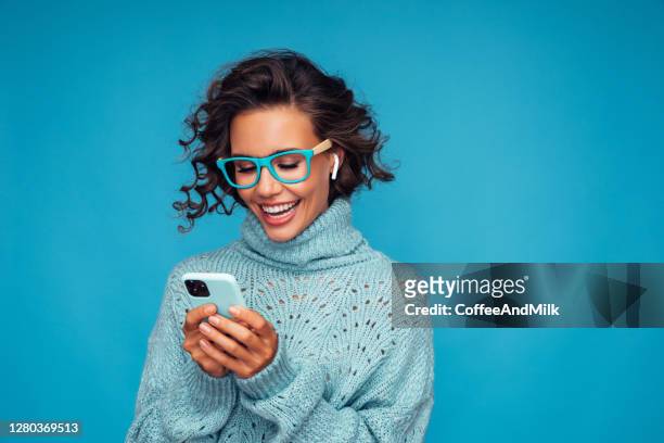 beautiful woman standing in front of blue background with smart phone - woman isolated imagens e fotografias de stock
