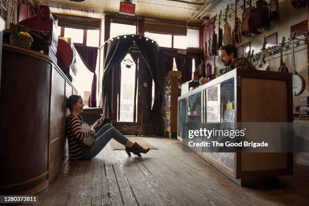 young woman sitting on floor of music shop strumming a banjo - musikgeschäft stock-fotos und bilder