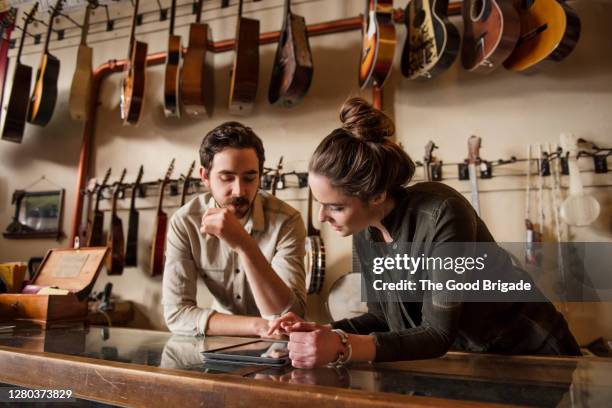 young couple working behind counter in music store - pequeña empresa fotografías e imágenes de stock