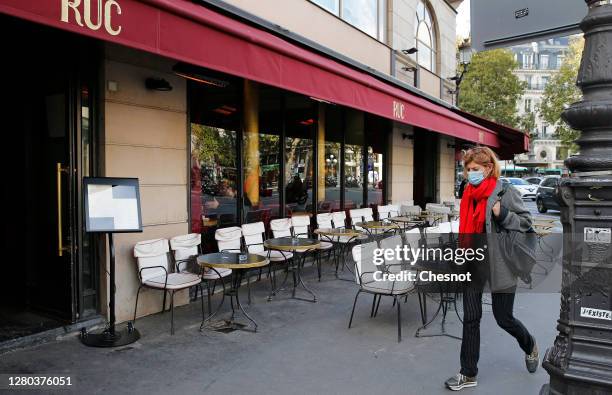 Woman wearing a protective face mask walks past an empty cafe terrace next to the Rue de Rivoli on October 15, 2020 in Paris, France. In the absence...