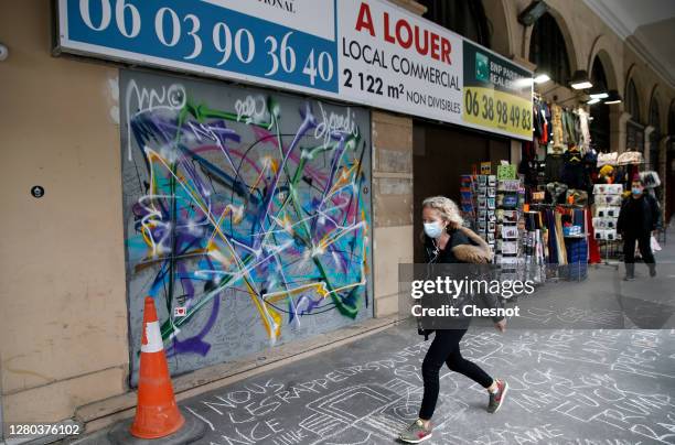 Woman wearing a protective face mask walks past a closed gift shop at a nearly empty Rue de Rivoli on October 15, 2020 in Paris, France. In the...