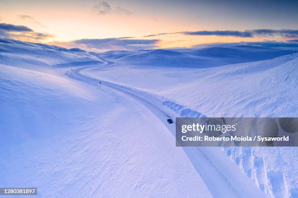 car traveling on scenic road in the snow at sunset, finnmark, norway - snow covered road stockfoto's en -beelden