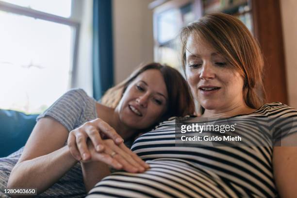 woman feeling pregnancy of her girlfriend. - prenatal care stock pictures, royalty-free photos & images