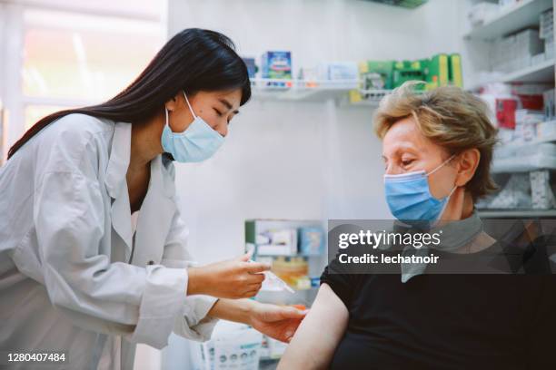 asian nurse giving flu vaccine to a senior patient - pharmacy vaccination stock pictures, royalty-free photos & images