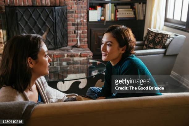 young woman talking with elder sister on sofa at home - zus stockfoto's en -beelden