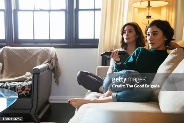sisters watching tv on sofa at home - watching stock-fotos und bilder