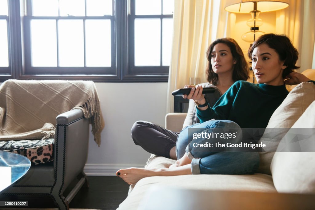 Sisters watching TV on sofa at home