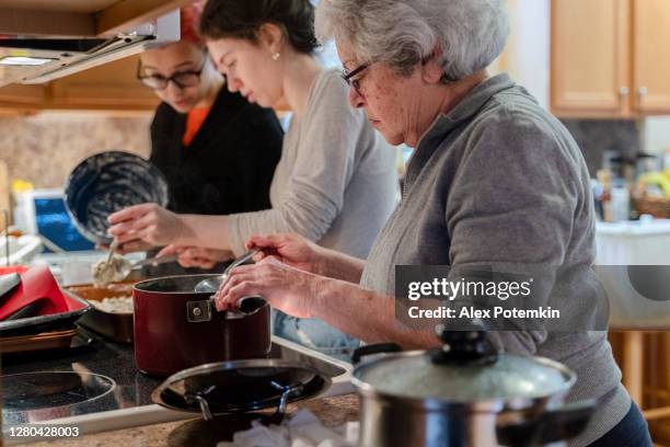 grandma cooking soup in her kitchen as her granddaughters make a pie alongside her - crowded kitchen stock pictures, royalty-free photos & images