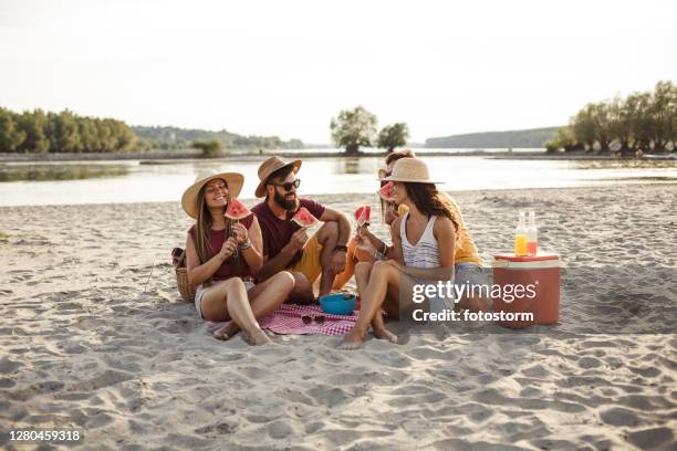 friends enjoying watermelon on a beach picnic - picnic friends stock pictures, royalty-free photos & images