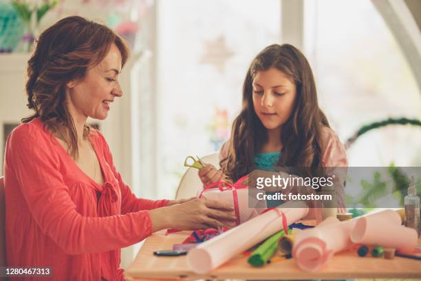 young girl assisting her mother tie a ribbon on a gift box - care package stock pictures, royalty-free photos & images