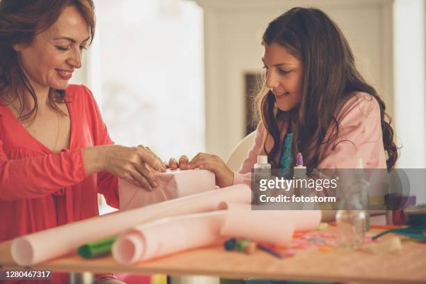 happy mother and daughter wrapping a present together - care package stock pictures, royalty-free photos & images