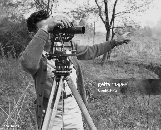 Surveyor pointing with his left hand while using a theodolite mounted on a tripod during the development of the Pan-American Highway, a network of...