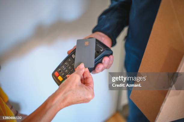 la donna anziana paga con carta di credito al fattorino anziano alla porta d'ingresso - consegna a domicilio foto e immagini stock