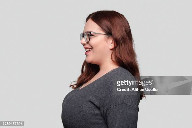 vista del profilo di una giovane donna allegra con occhiali che distogliano con un'espressione facciale sorridente su sfondo grigio - vista laterale foto e immagini stock