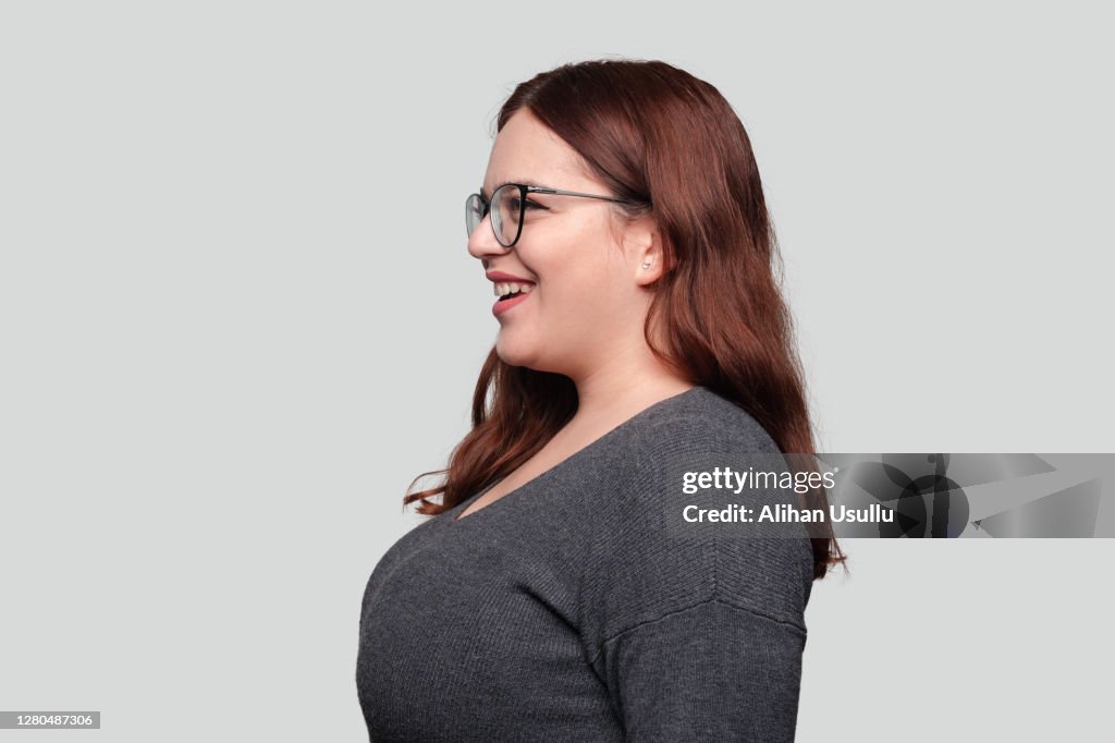 Visão de perfil de jovem alegre com óculos olhando para longe com expressão facial sorridente sobre fundo cinza