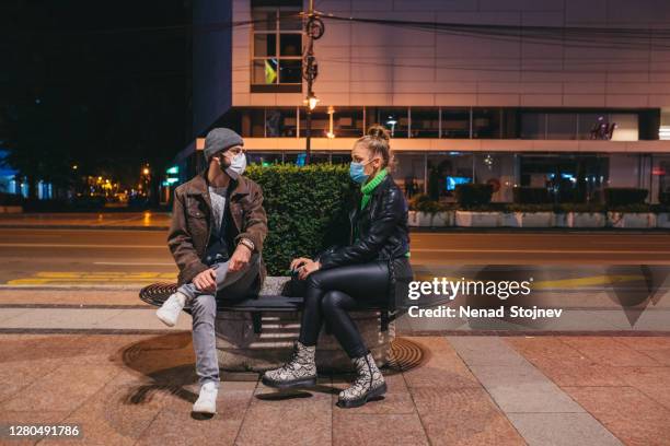 young caucasian friends with n-95 masks are talking at the bus station and waiting for the bus - jan 19 stock pictures, royalty-free photos & images