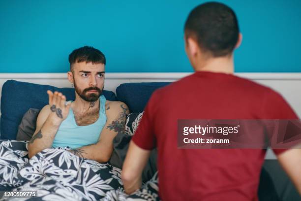 looking at his boyfriend and gesturing, having an argument in bed - sad gay person stock pictures, royalty-free photos & images