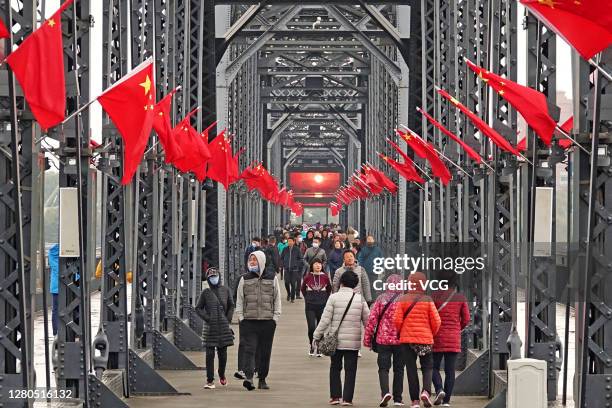 Tourists walk on the Broken Bridge decorated with Chinese flags over the Yalu river on October 15, 2020 in Dandong, Liaoning Province of China.