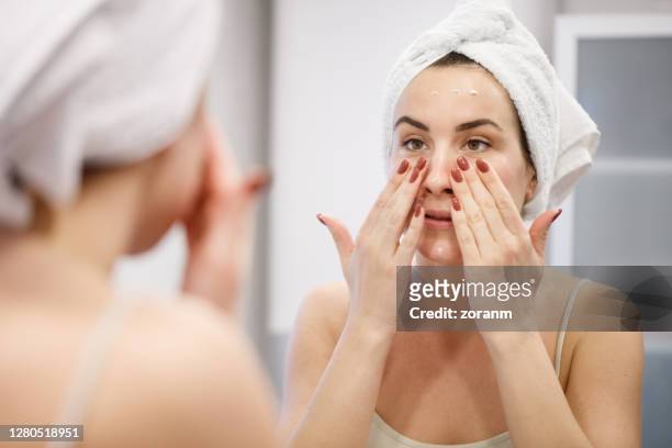 reflexion der frau mit handtuch auf dem kopf verbreiten gesicht creme - gesicht kosmetik maske stock-fotos und bilder