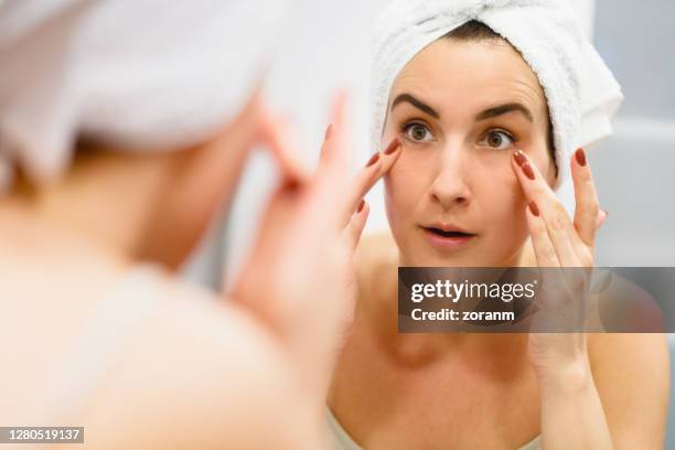 reflection of woman with towel on hair grimacing and touching facial skin - tighten stock pictures, royalty-free photos & images